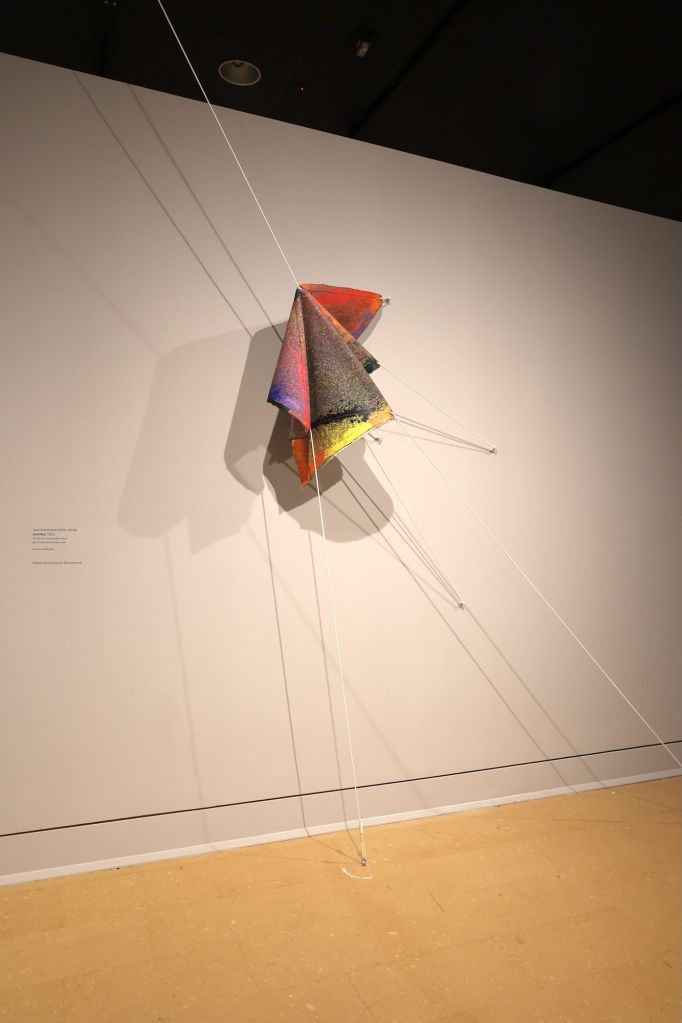 An art piece is displayed folded in on itself and held in place by multiple strings