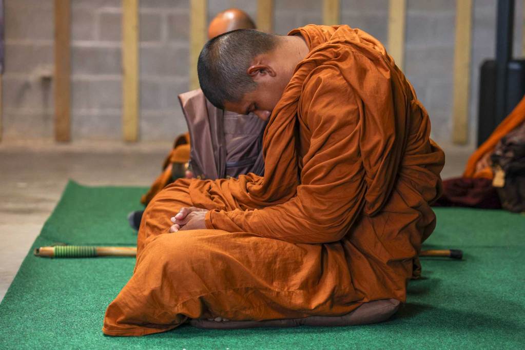 A monk in orange robes sits upright, curled on himself in meditation