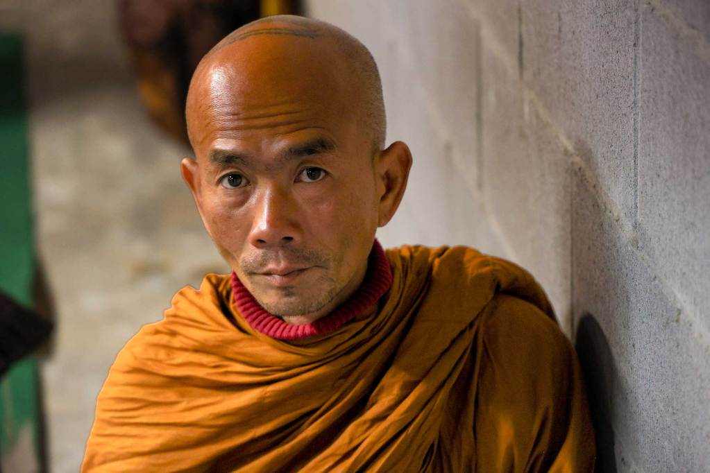 A closeup of a monk in orange robes sitting inside a simple room