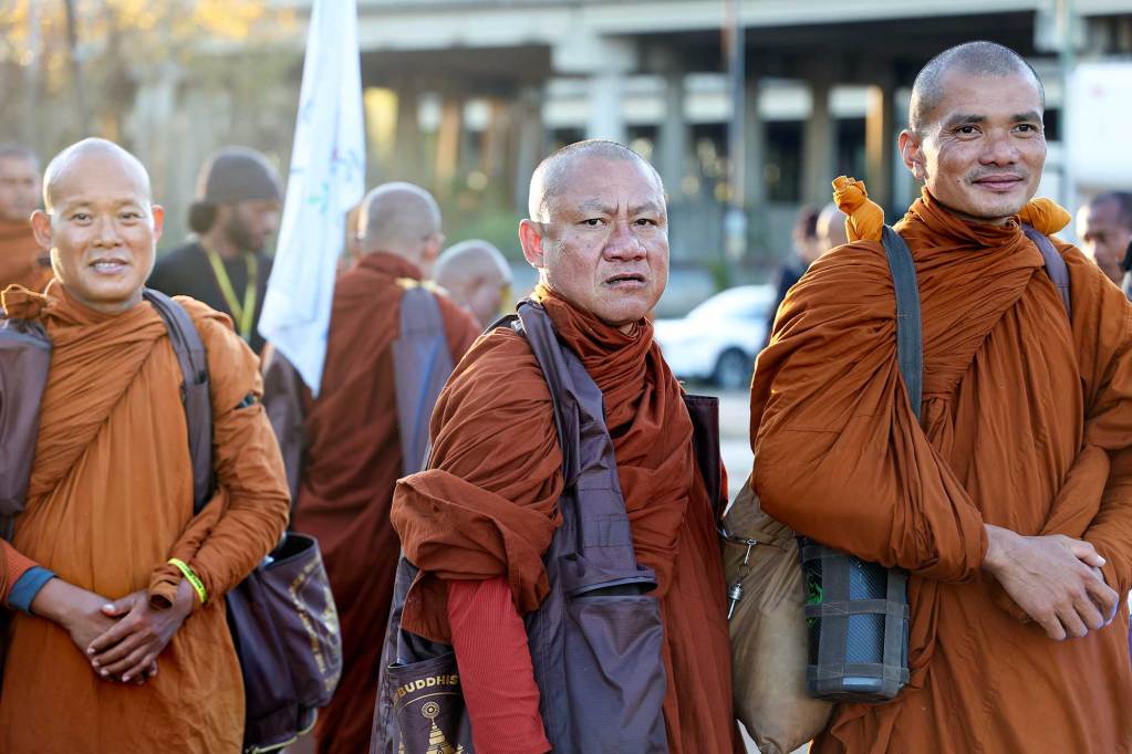 A line of monks in orange robes prepare to walk down a road with a police escort