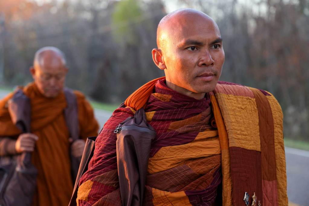 A line of monks in orange robes walk down a paved road in Mississippi