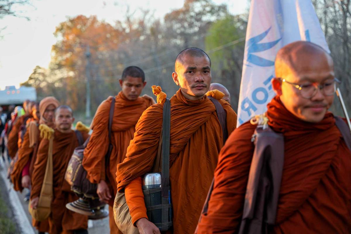 A line of monks in orange robes walk down a paved road in Mississippi