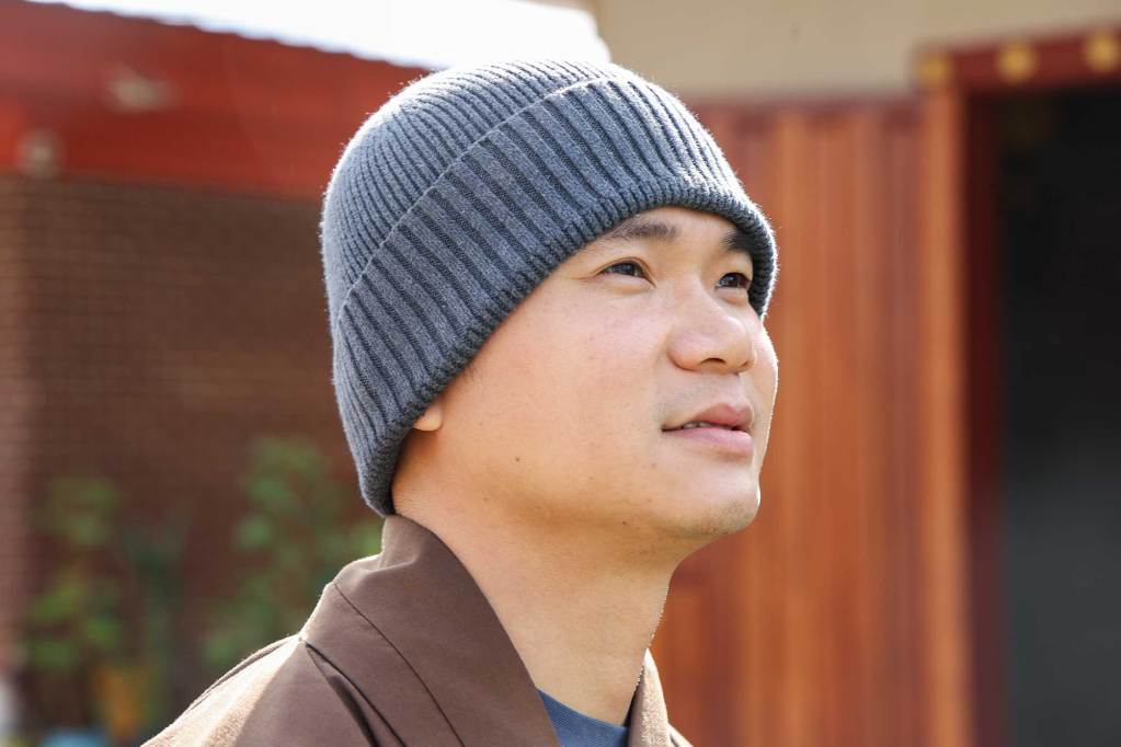 A closeup of a monk standing outside with a warm hat on