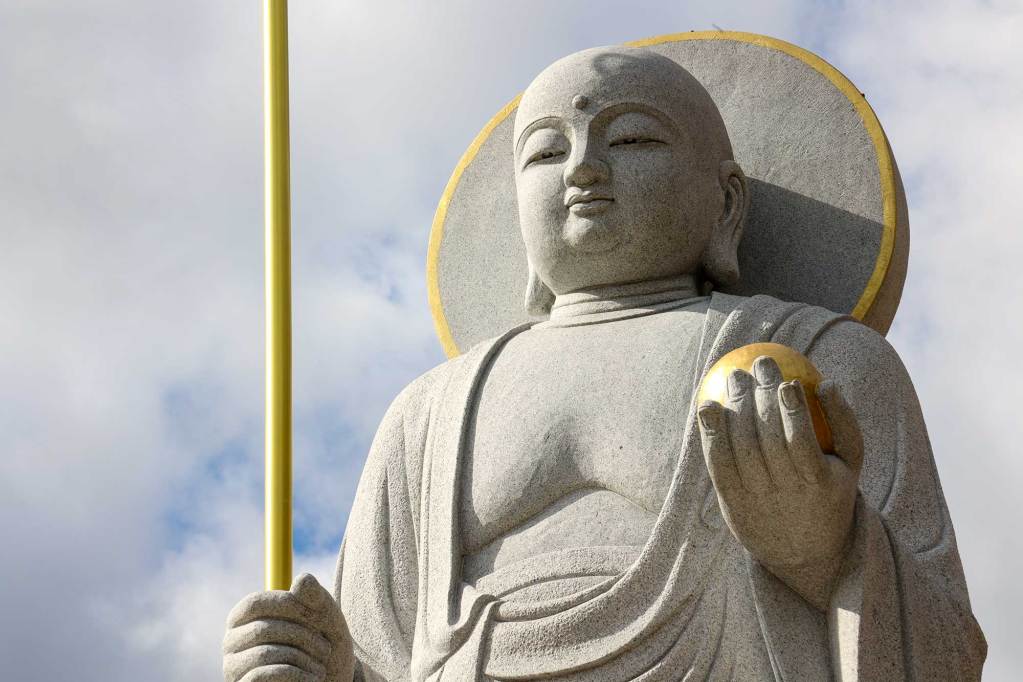 A large concrete Buddha statue outside on an overcast day, sunlight shining on golden highlights