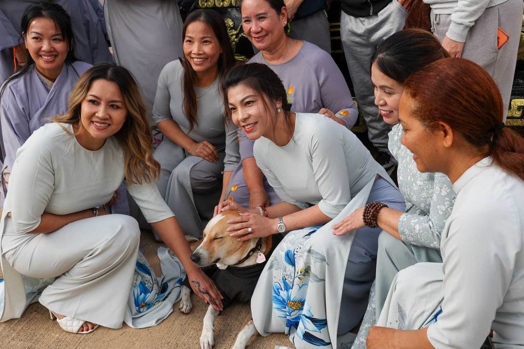 Women from a local temple pose with a white and orange dog