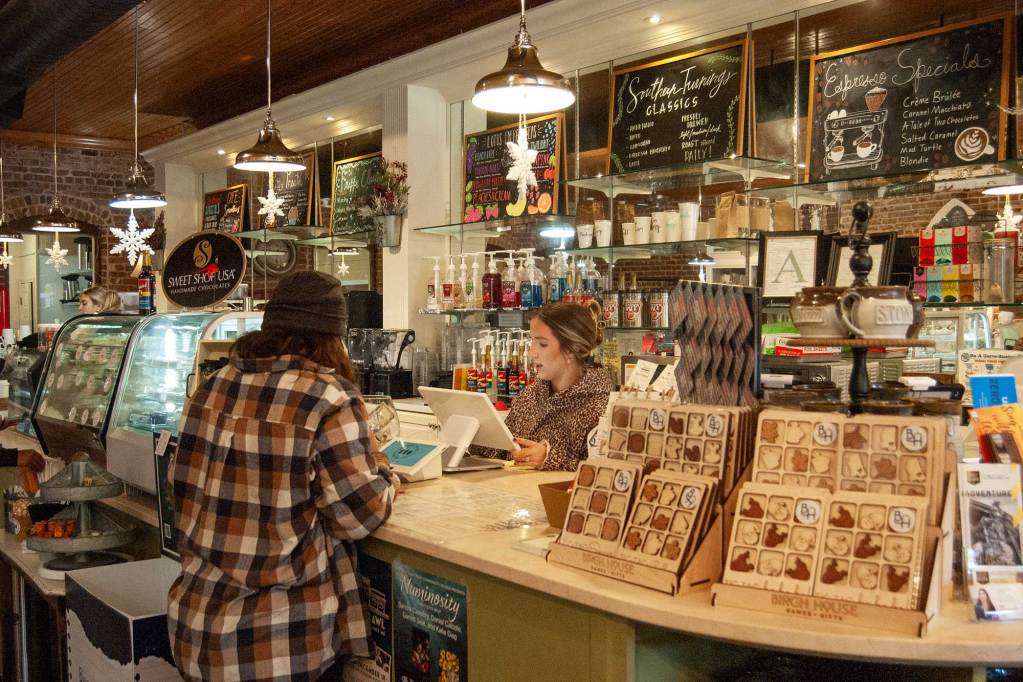 A barista stands behind a counter taking an order inside a coffee shop filled with products and displays