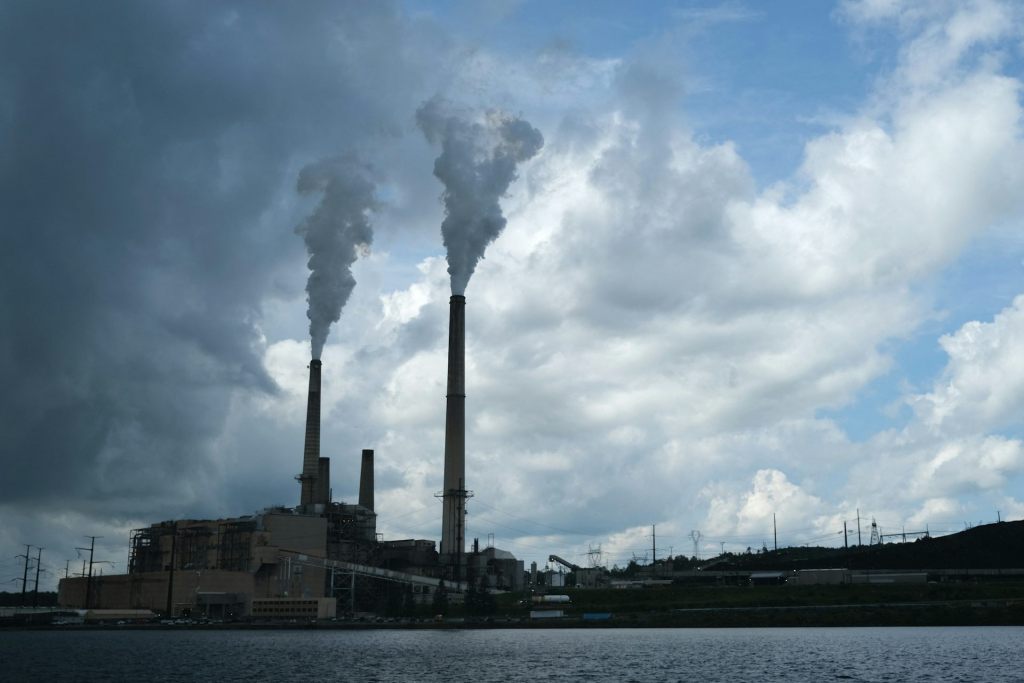 A factory with smoke billowing out of its smokestacks against a darkened, overcast sky.