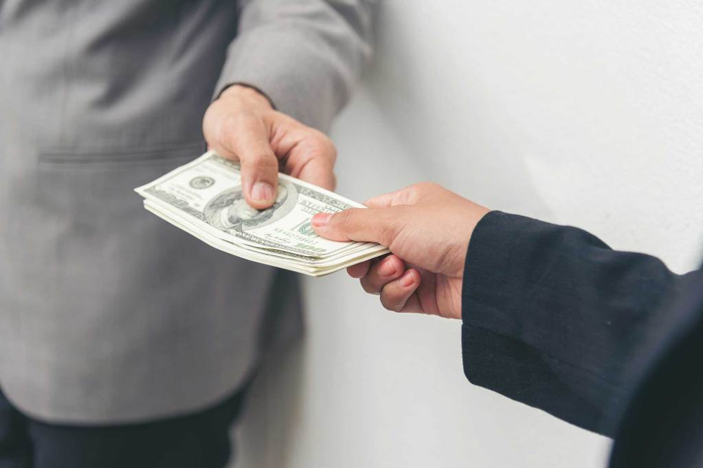 A hand handing a stack of cash to another person