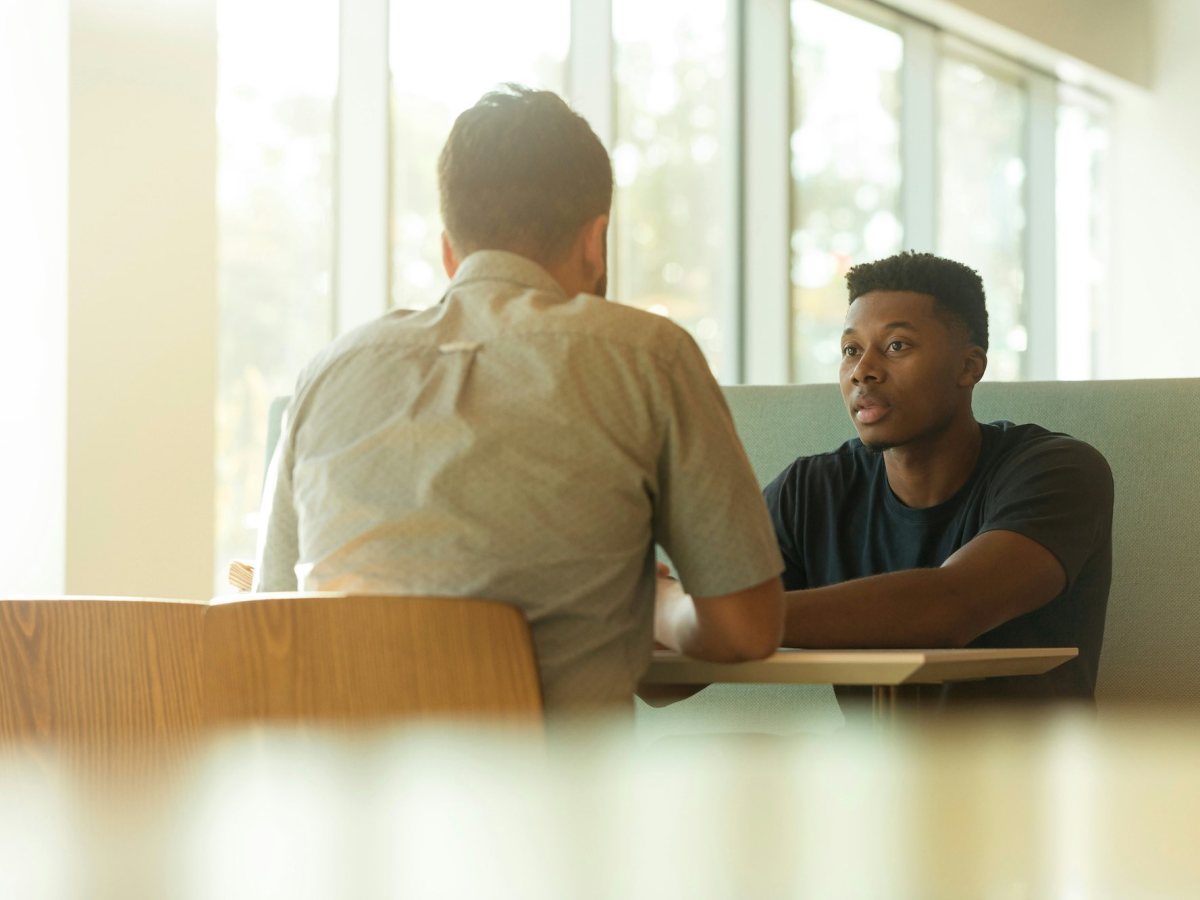 Two men seated at a table talking, one with his back to the camera