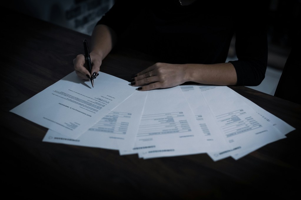 A woman writing on several documents on a table.