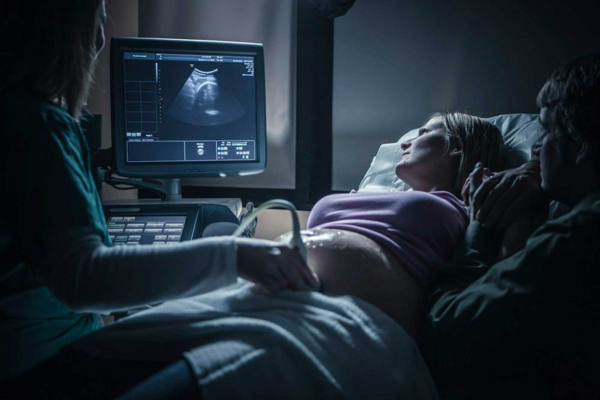 A woman on a hospital bed receiving an ultrasound from a doctor.