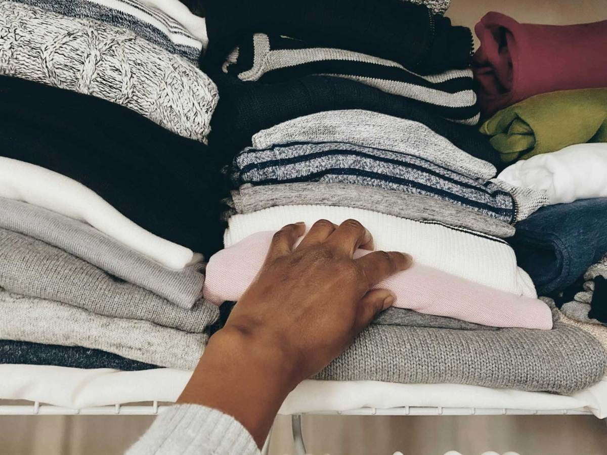 A hand grabbing a sweater out of a stacked pile on a closet shelf