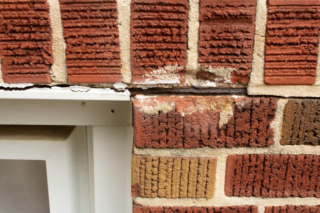 A prominent crack in a brick wall next to a window.