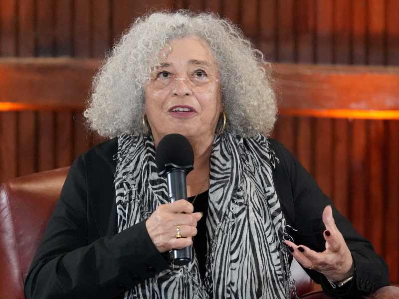 Angela Davis, in black with a zebra print scarf, speaks to an audience