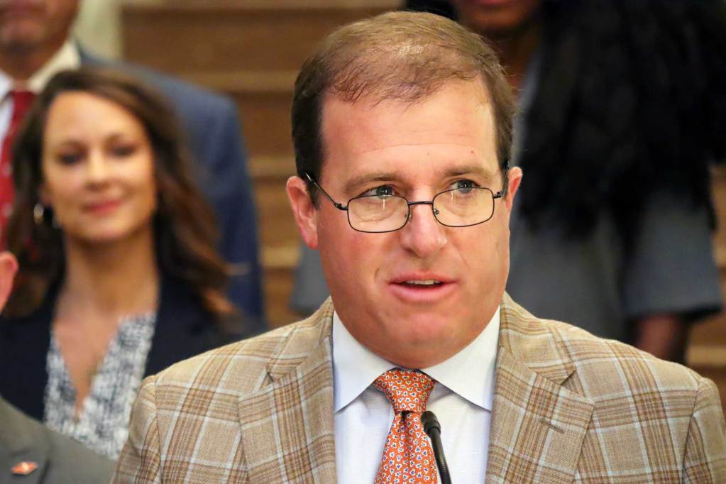 Josh Harkins in a brown patterned suit speaks at a press conference