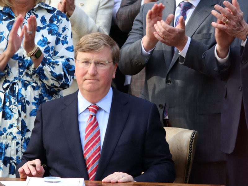 Governor Tate Reeves seated, ready to sign a bill as others watch and clap