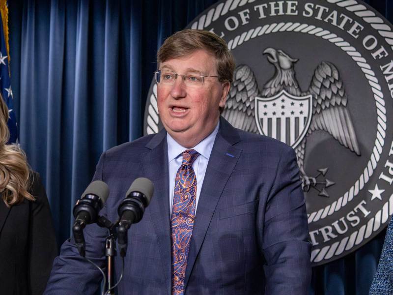 Tate Reeves speaking at a lectern in front of the seal of Mississippi