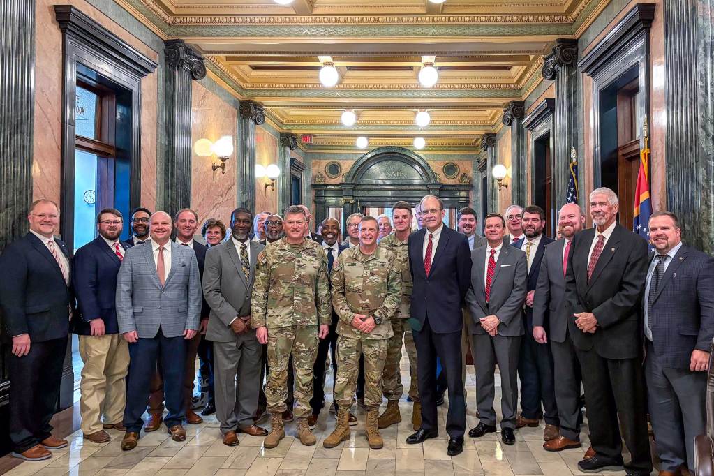 A group of officials line up with some men in army fatigues at the capitol