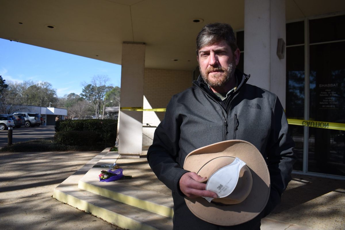 A man, hat in hand, speaks on the taped-off steps of Beth Israel Congregation