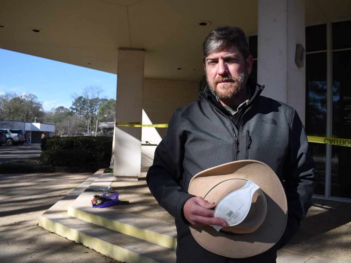 A man, hat in hand, speaks on the taped-off steps of Beth Israel Congregation