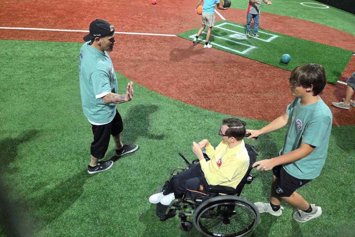 A volunteer pushes a wheelchair user on a field as another participant raises a hand for a high five.