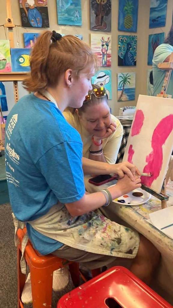 A participant and her mother paint together at a studio table during a Buddy Sports art activity.