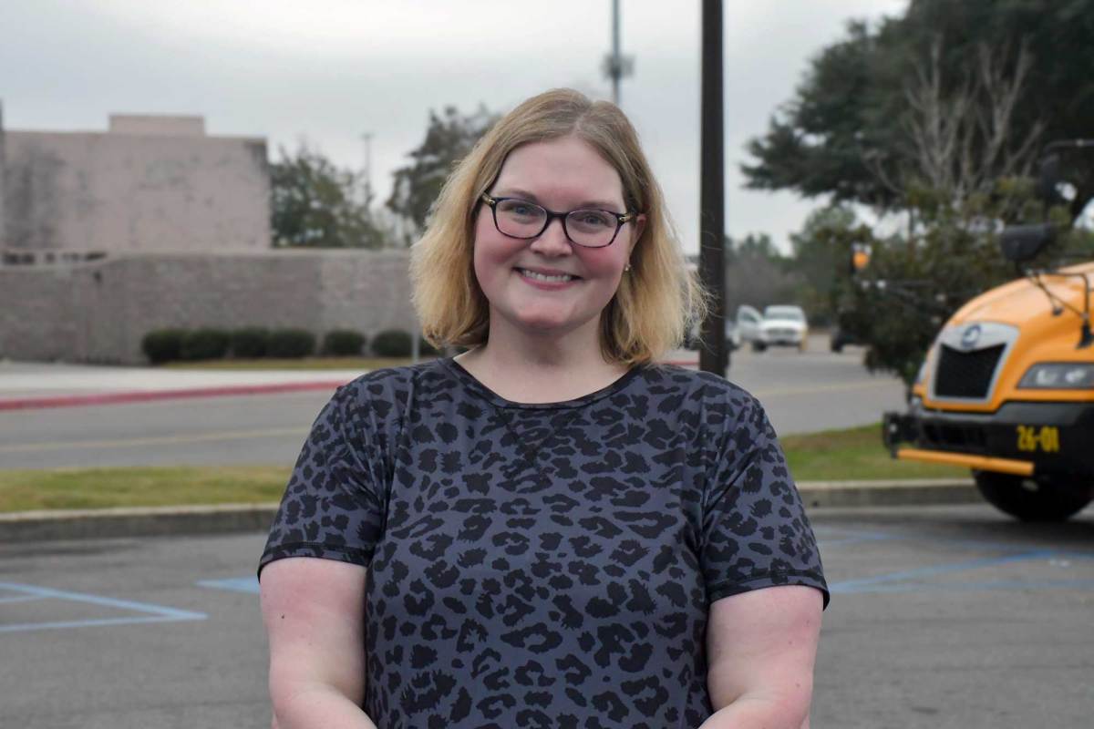 Woman wearing a grey and black leopard print short-sleeve shirt stands in mall parking lot smiling.