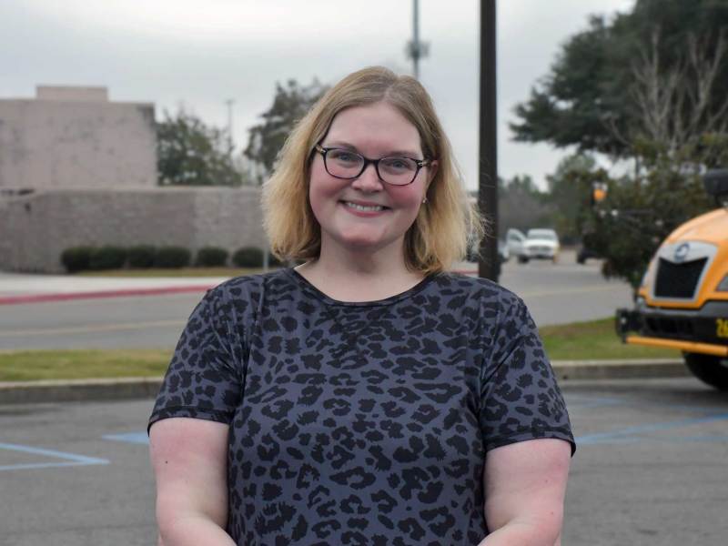 Woman wearing a grey and black leopard print short-sleeve shirt stands in mall parking lot smiling.