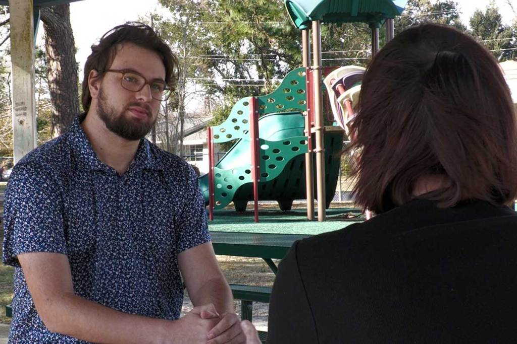 Over the shoulder image of a woman across a picnic table talking to a reporter.