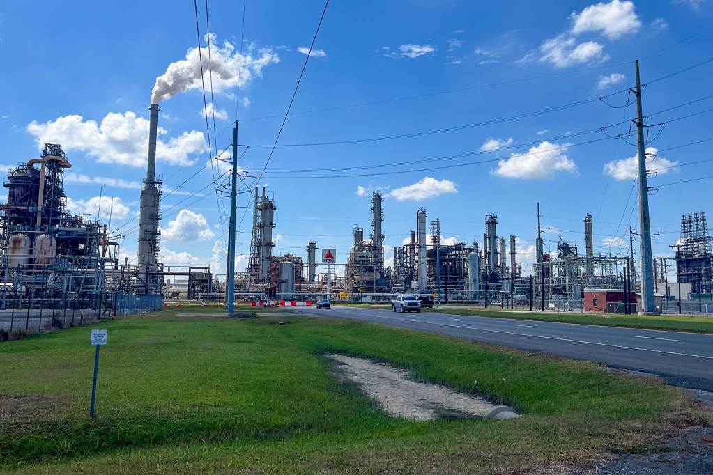 A large oil refinery. Smoke billows from one of the smokestacks.