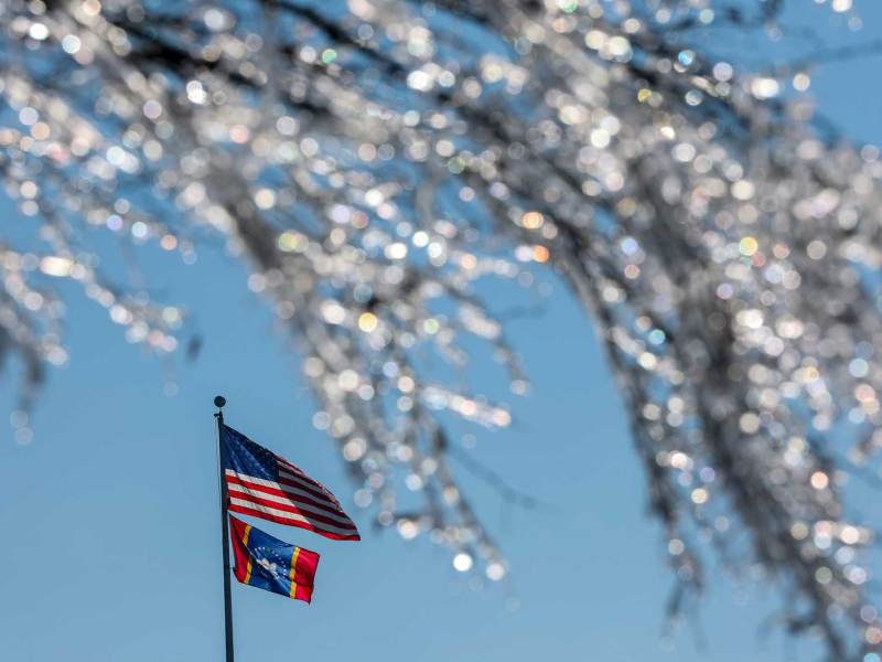 A flagpole with both the US Flag and MS Flag as seen past a tree frosted with ice