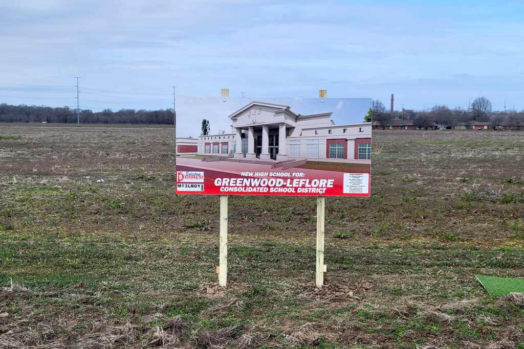 A plot of land with a sign showing a school building, labeled 'New High School For: Greenwood-Leflore Consolidated School District'