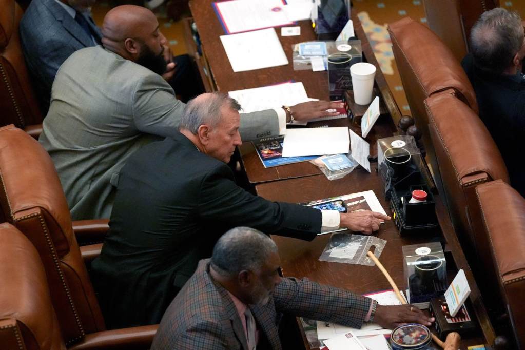 Three members of the house of representatives reach to push their attendance buttons at their chamber seats