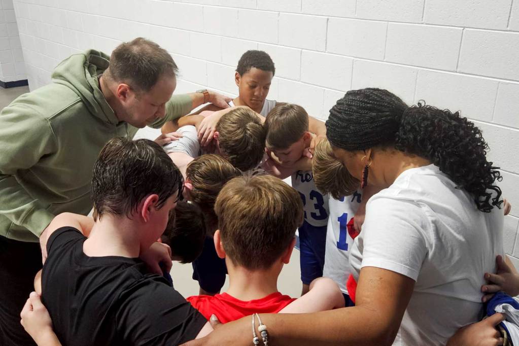 Torsheta Jackson and a coach huddle together in a circle with student athletes