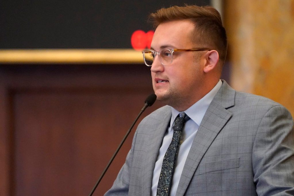 Jansen Owen, in a grey suit, speaking at a mic