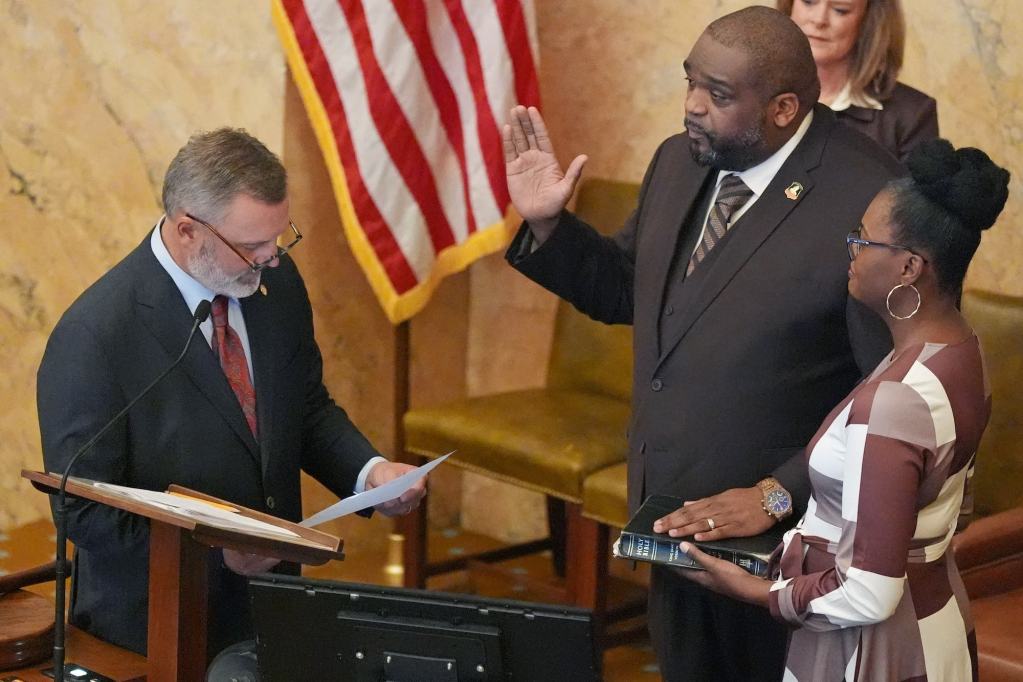 Justin Crosby holds one hand up and one hand on a bible held by his wife