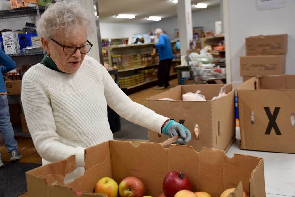 An older woman wearing a sweater and gloves sorts through produce in boxes