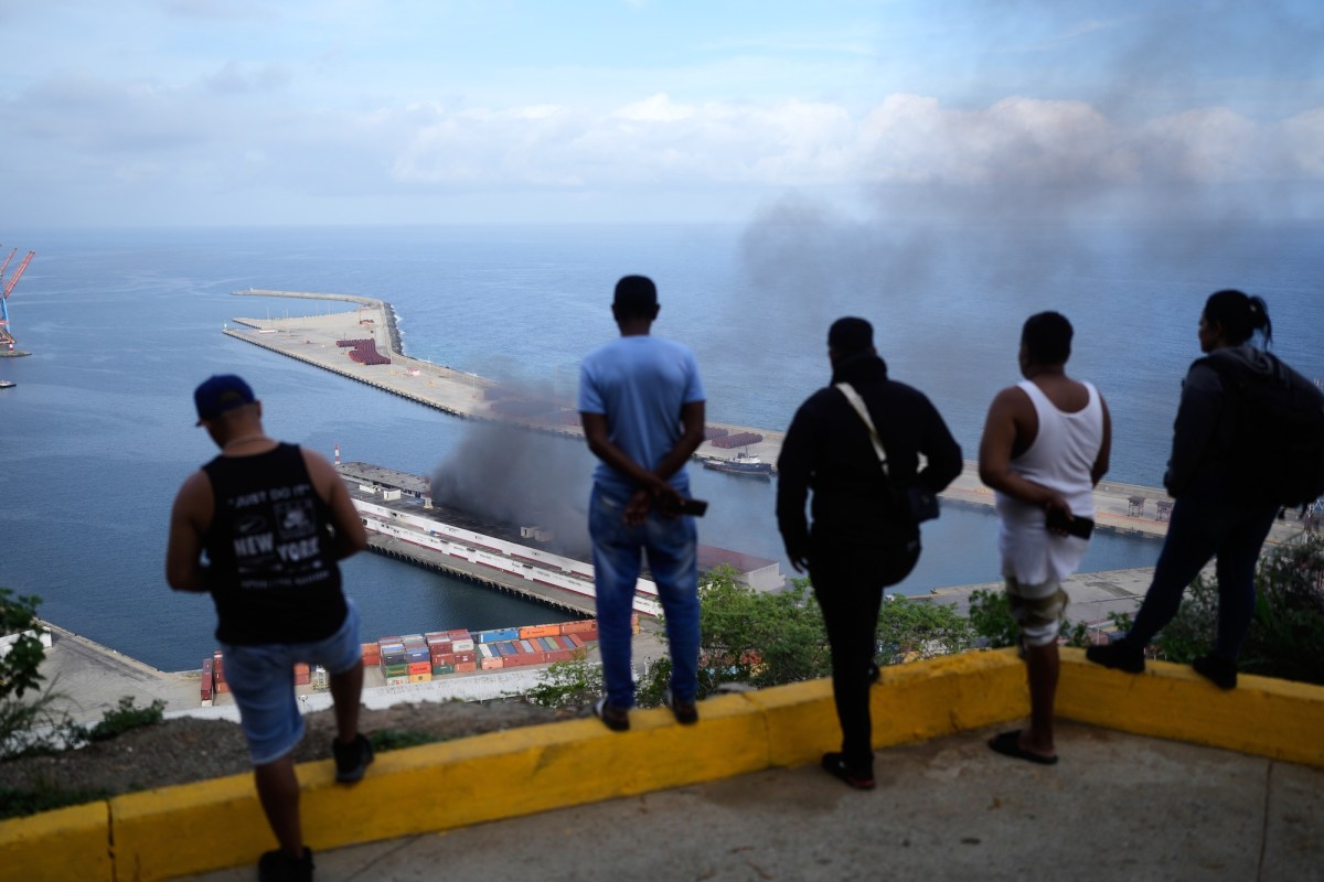 Several men watch as smoke billows from a pier near the water below them.