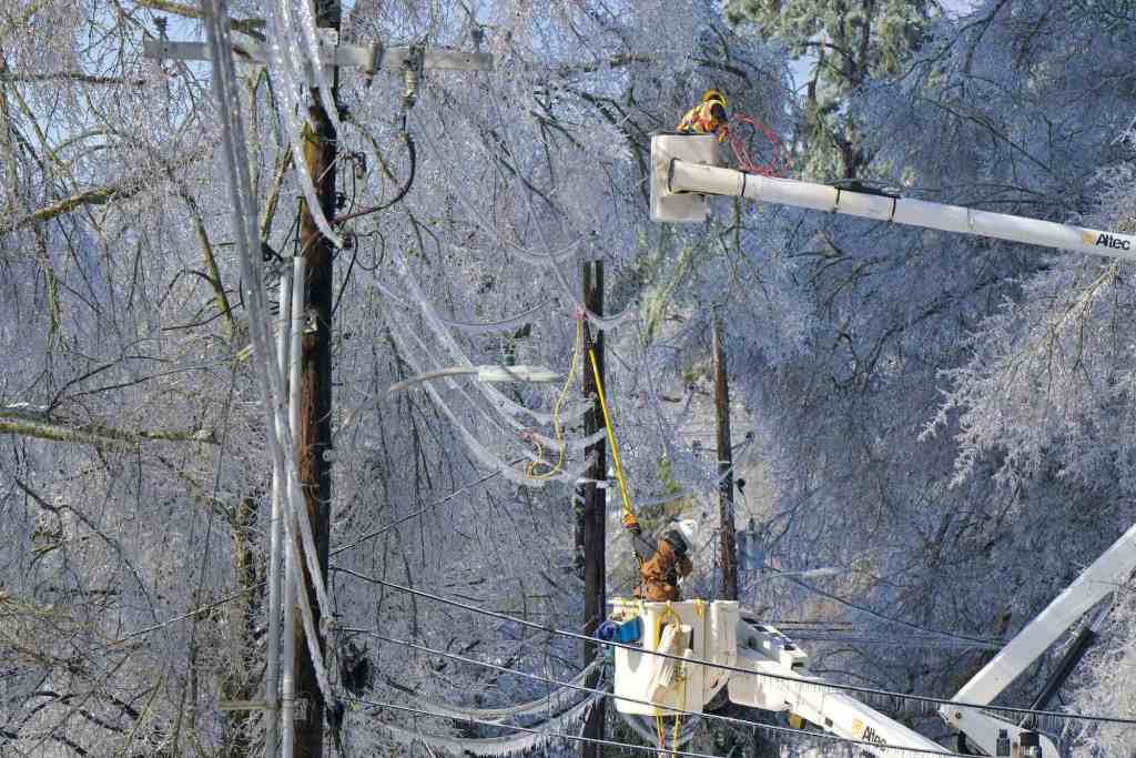Two linemen in truck buckets work on frozen lines in the winter