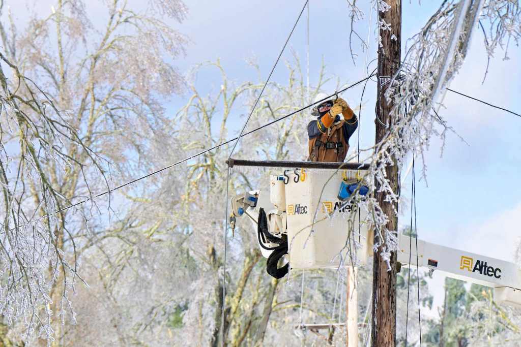 A lineman in a bucket works on lines surrounded by ice covered trees