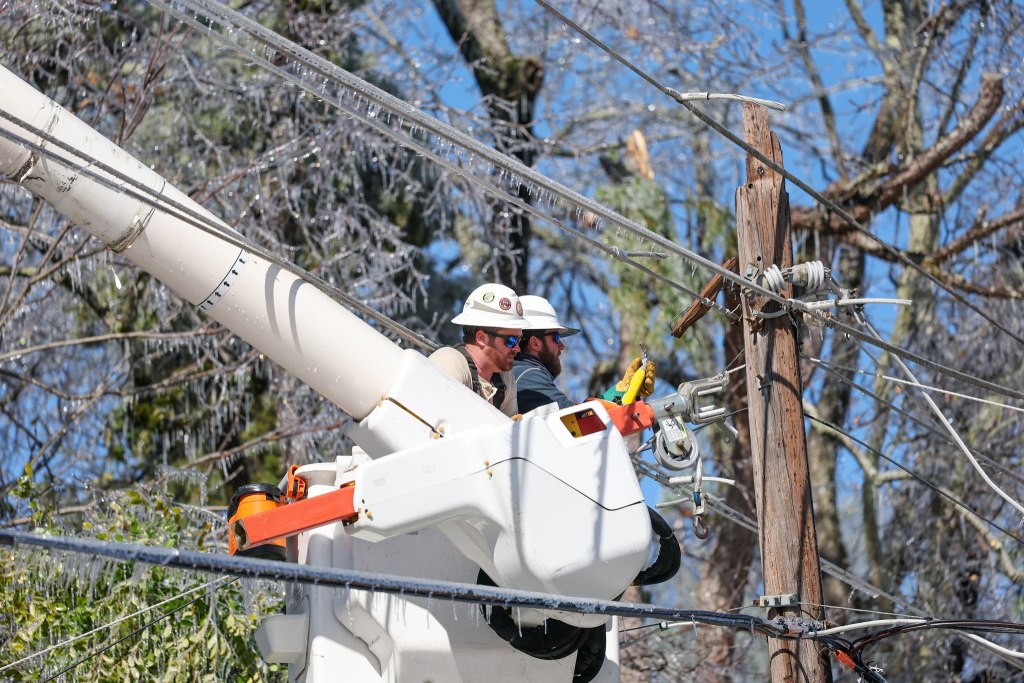 Two men in a utility bucket working on a utility pole. Icicles are hanging from the power lines.
