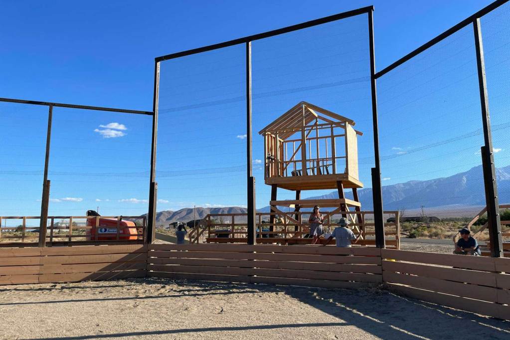 An announcers booth under construction behind a backstop on a baseball field.