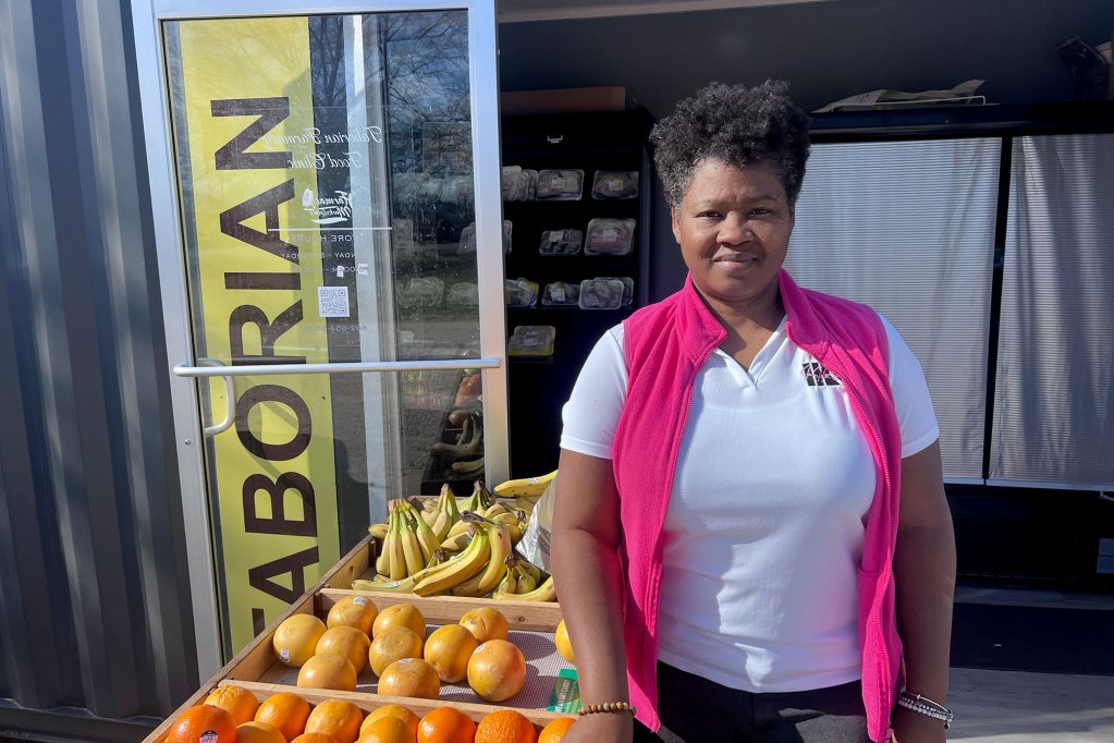 A woman stands beside a fruit stand