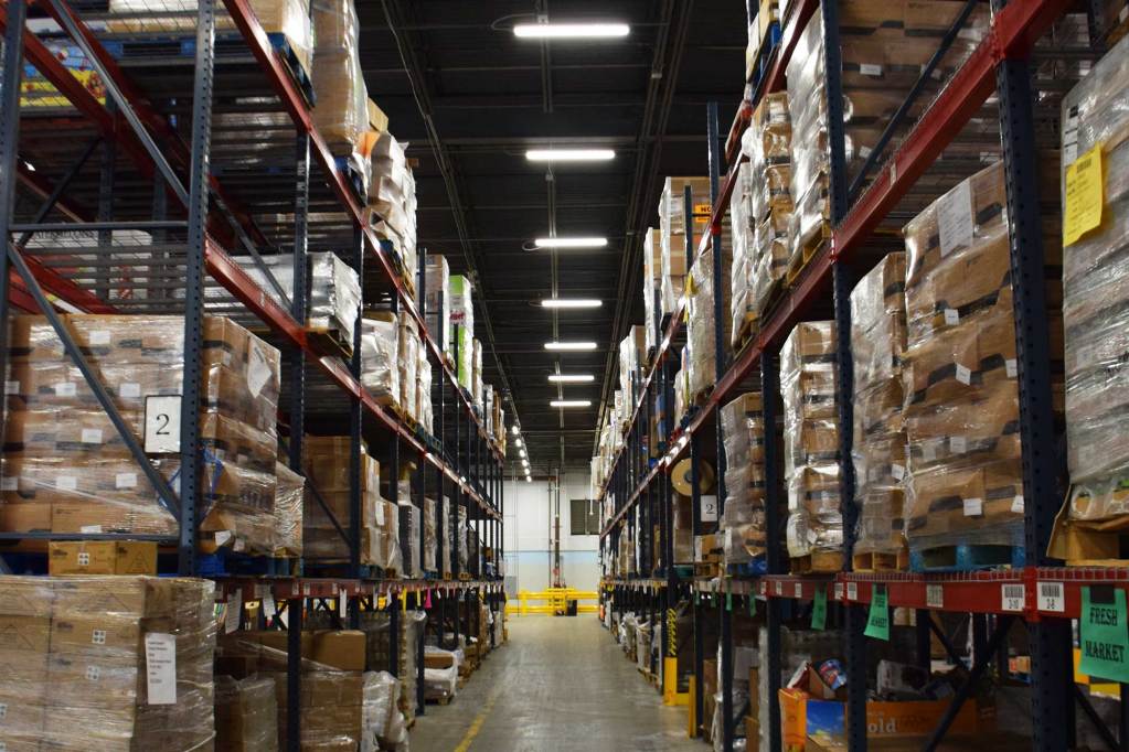 A view between tall rows of shelves containing pallets of food