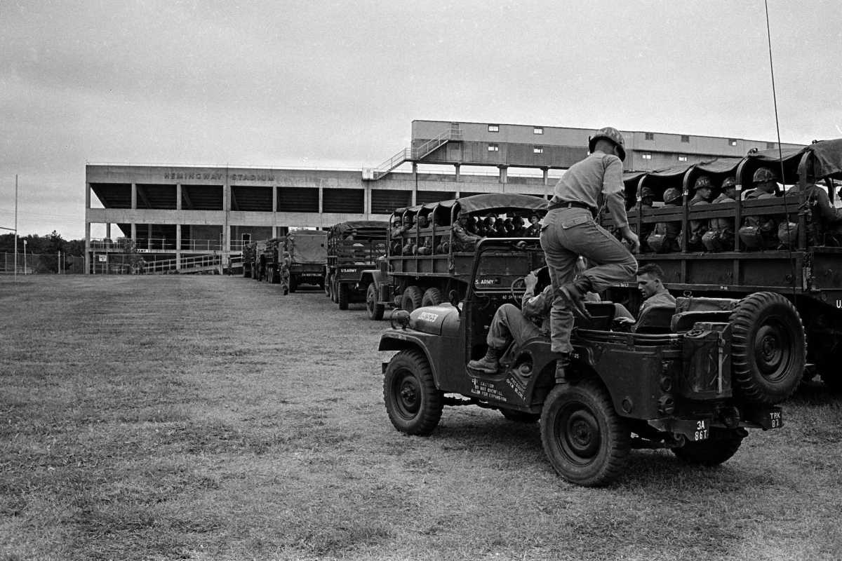 A black and white photo showing military jeeps filled with people on a university campus
