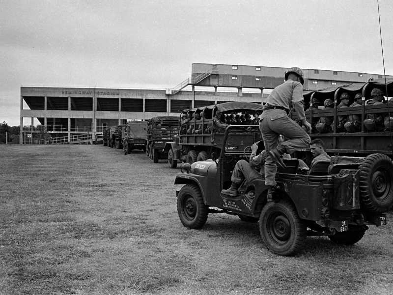 A black and white photo showing military jeeps filled with people on a university campus