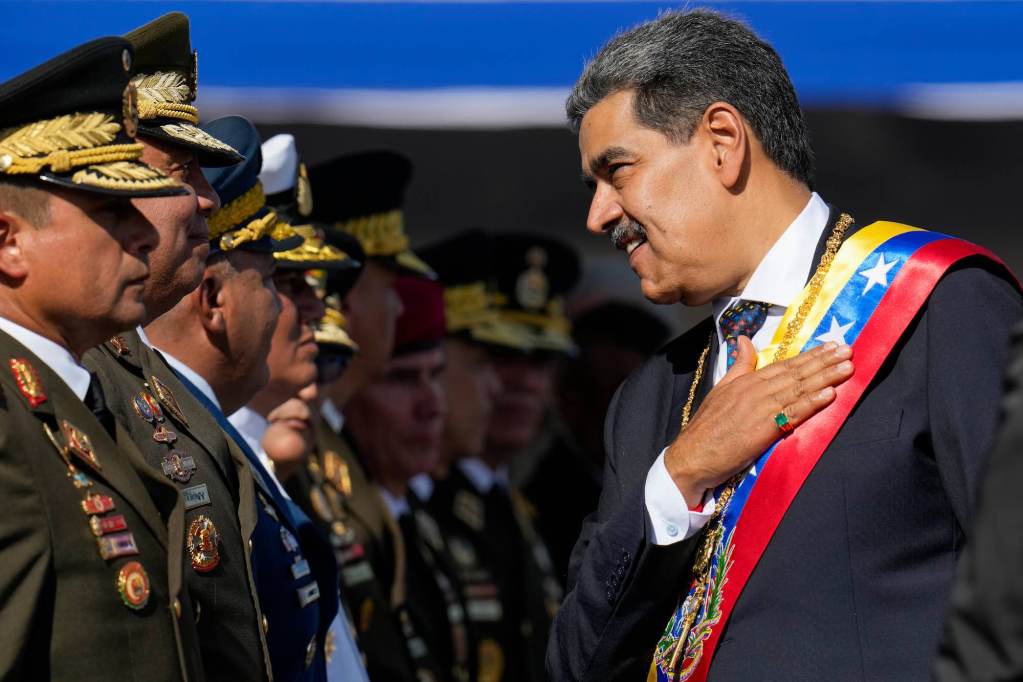 A man in a suit and colored sash with his hand on his chest greeting a man in a military uniform.