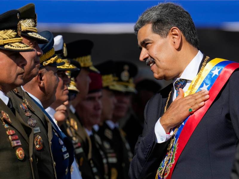 A man in a suit and colored sash with his hand on his chest greeting a man in a military uniform.