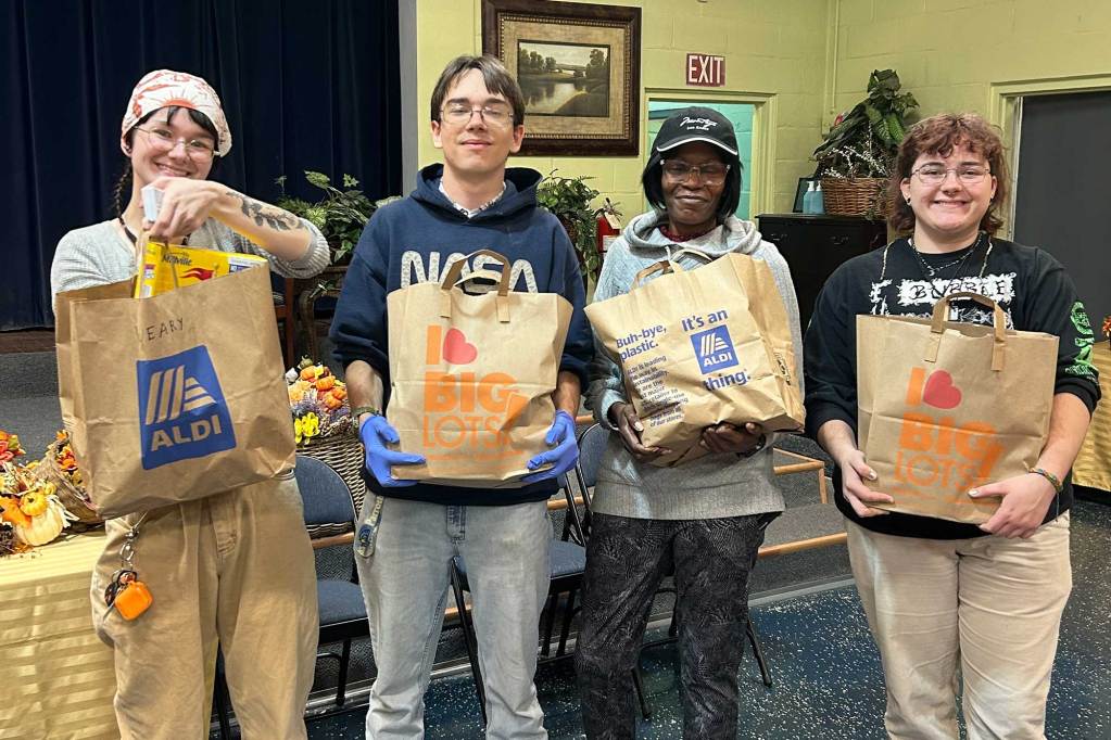 Four people hold up bags of donated food items