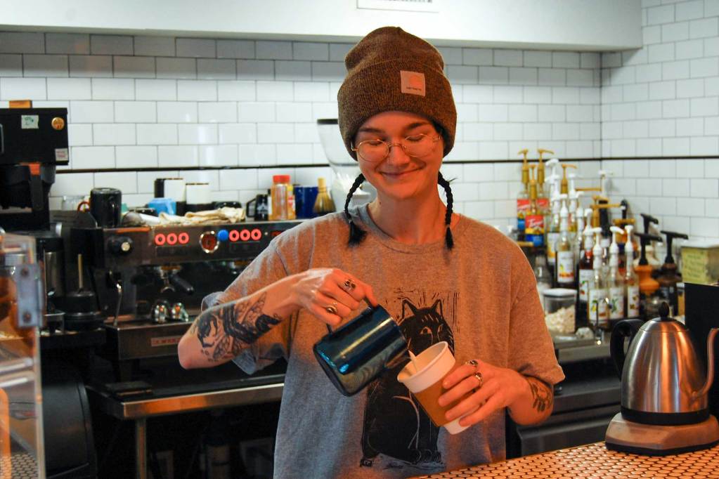 A woman makes coffee behind the bar of a coffee shop